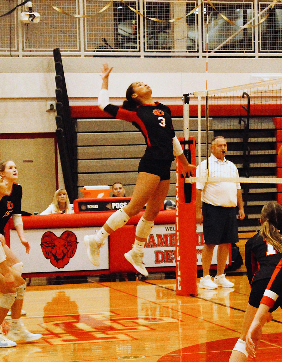 Senior girls volleyball player mid-jump prepared to spike at the net.