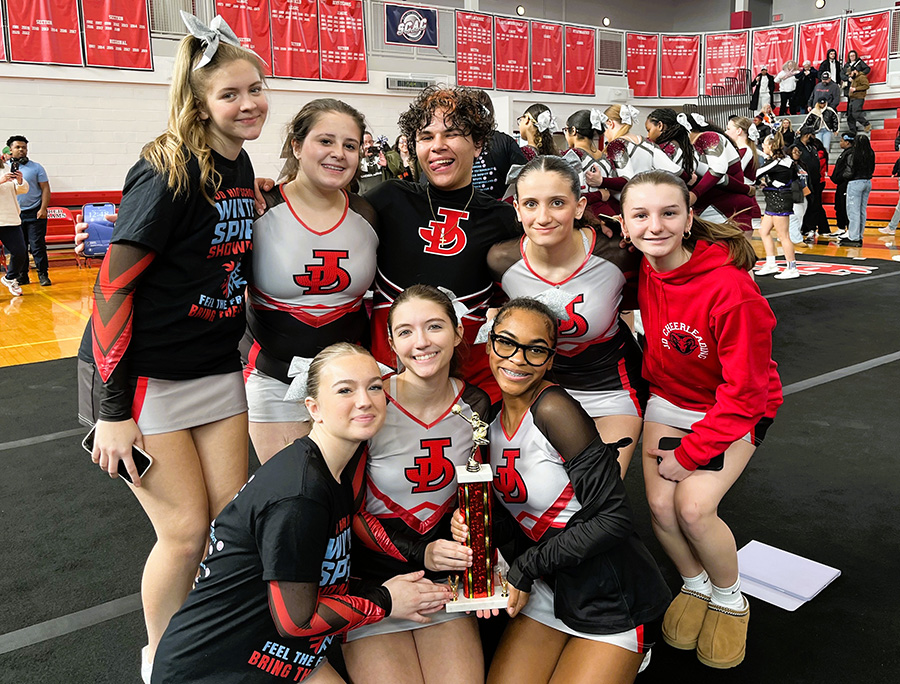 J-D Cheerleaders pose for group photo in gym while holding trophy.