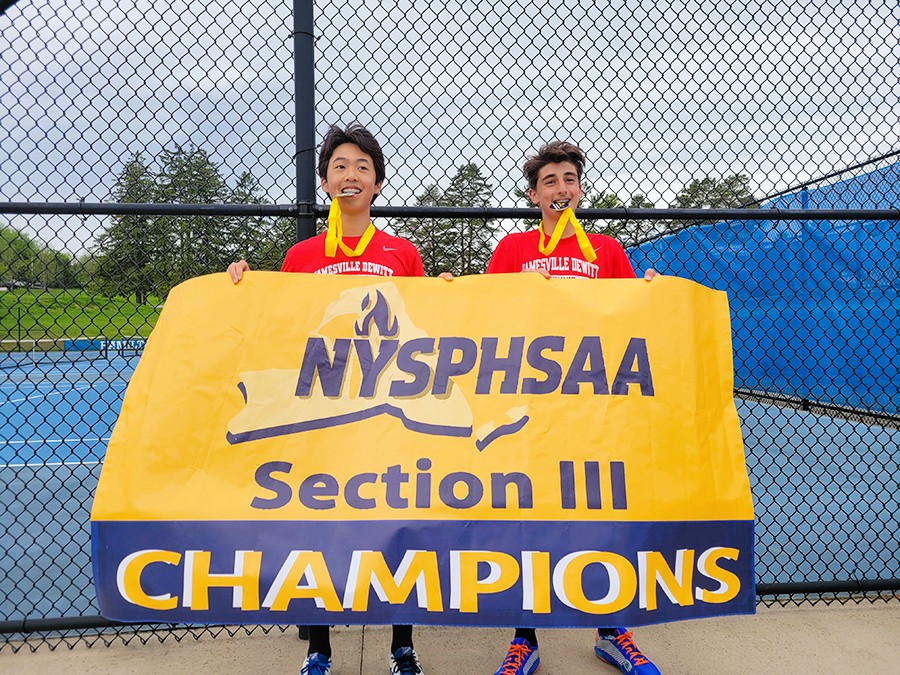 Fouad Farah and Alwin Lu hold Section III Division II boys tennis doubles championship banner with medals in their mouth.