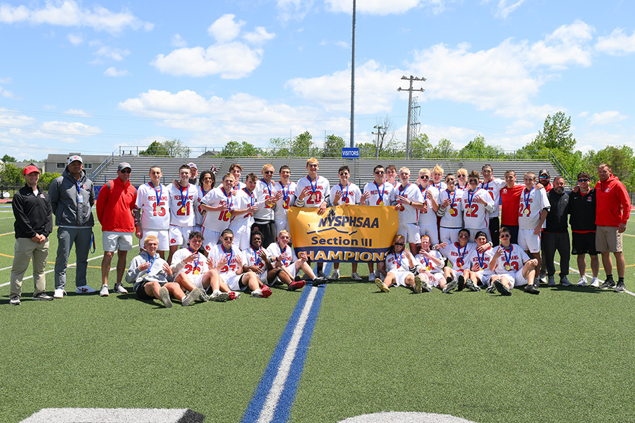 Boys lacrosse team post for group photo with championship banner.