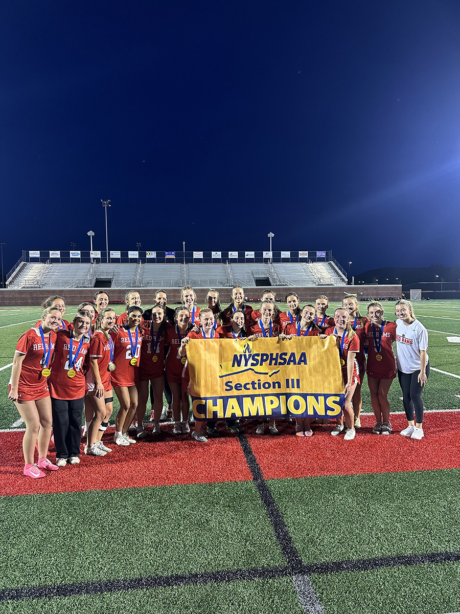 Girls lacrosse team post for group photo with championship banner.