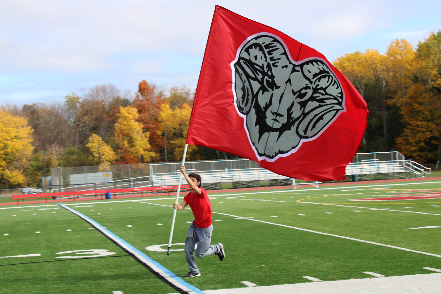 Close up of student running on turf field holding flag up.
