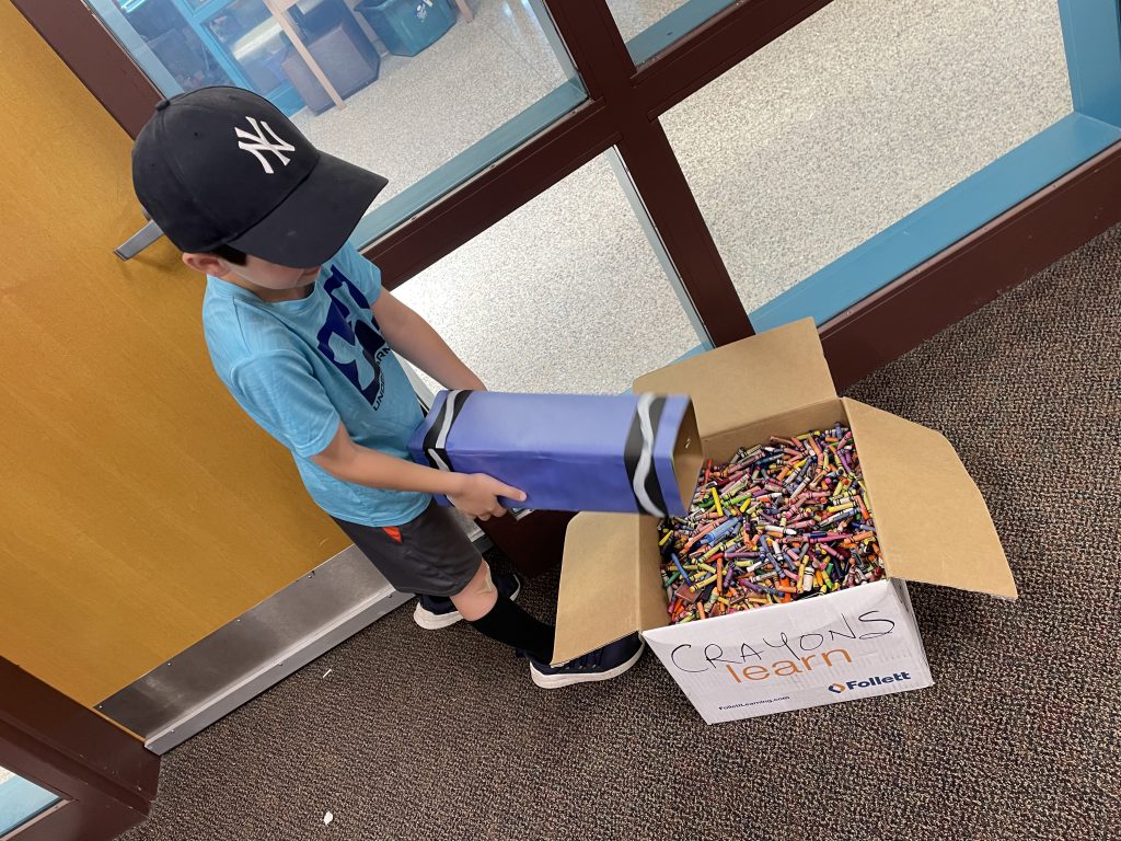 Photo of student pouring crayons into box. 