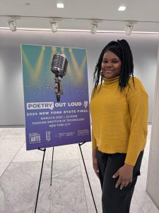 Photo of Anadia St. James standing next to Poetry Out Loud competition banner. 