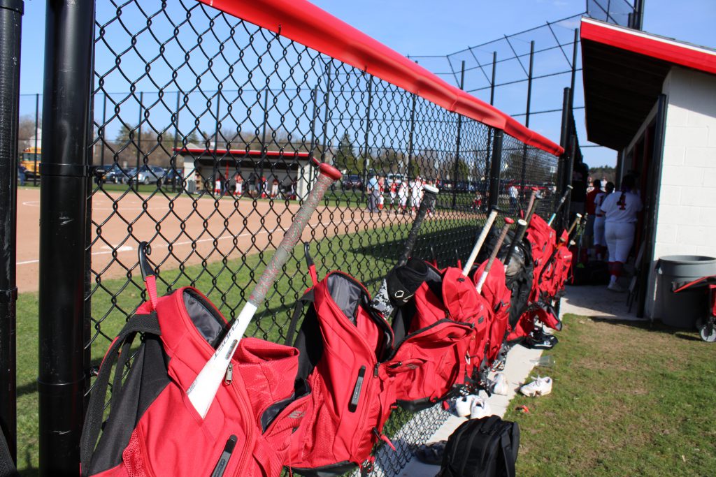 Image of softball player gear along fence.