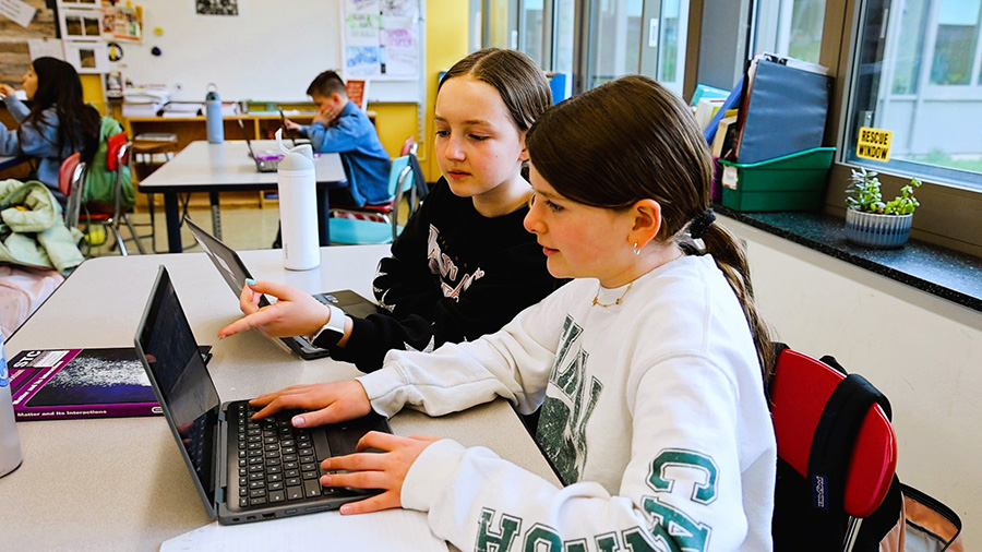 Middle school students work on laptops in classroom.
