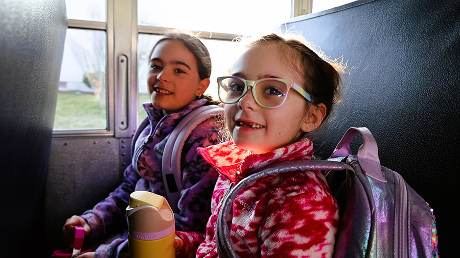 Two elementary students smile for camera while sitting in bus seat.