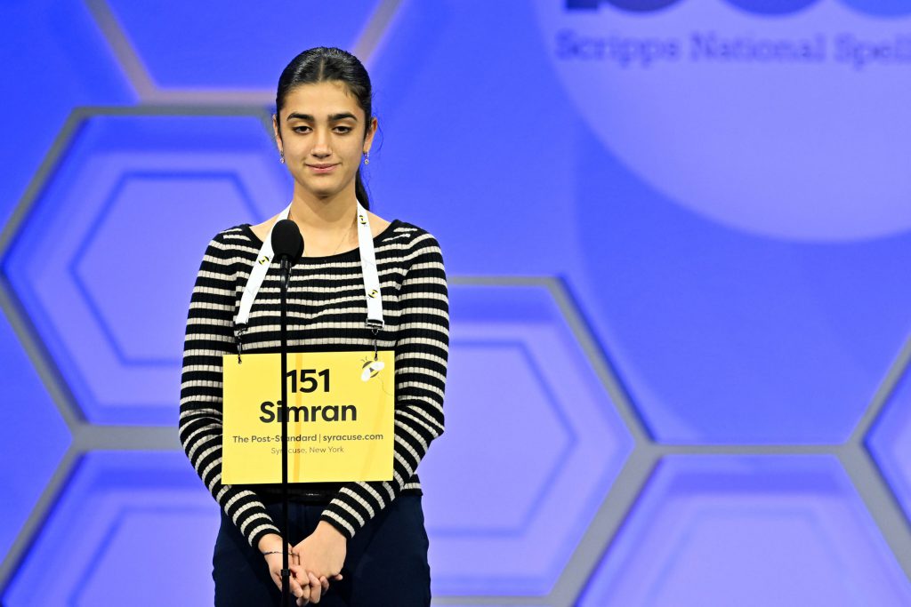 Simran Sanders competes in Scripps National Spelling Bee with sign hanging in front of her.
