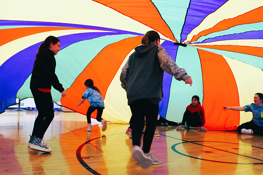 Third grade students play inside rainbow parachute during gym class.