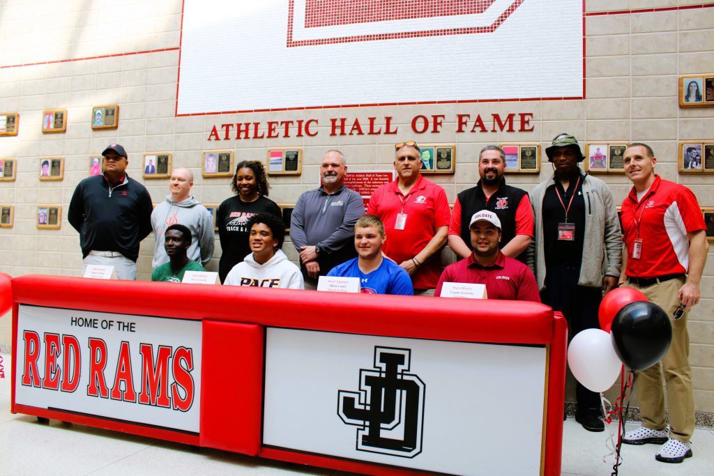 Four student-athletes pose for group photo with coaches for national letter of intent signing.