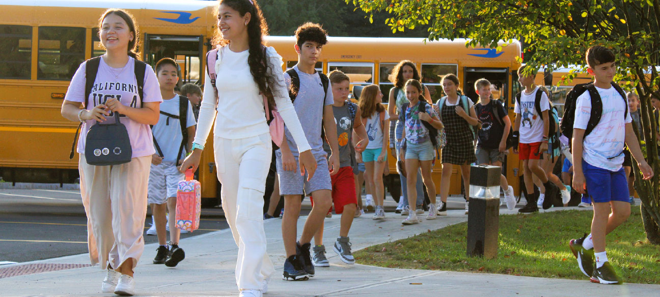 several students disembarking from school buses and walking on sidewalk