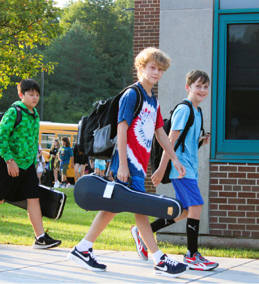 Middle school students walking on sidewalk carrying music instruments