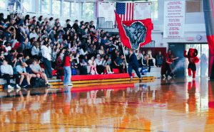 a high school student running with the school flag in a gymnasium pep rally