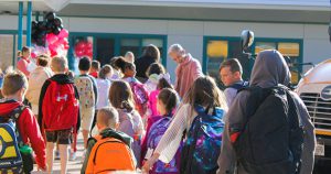 several elementary students unloading fomr buses and entering the building
