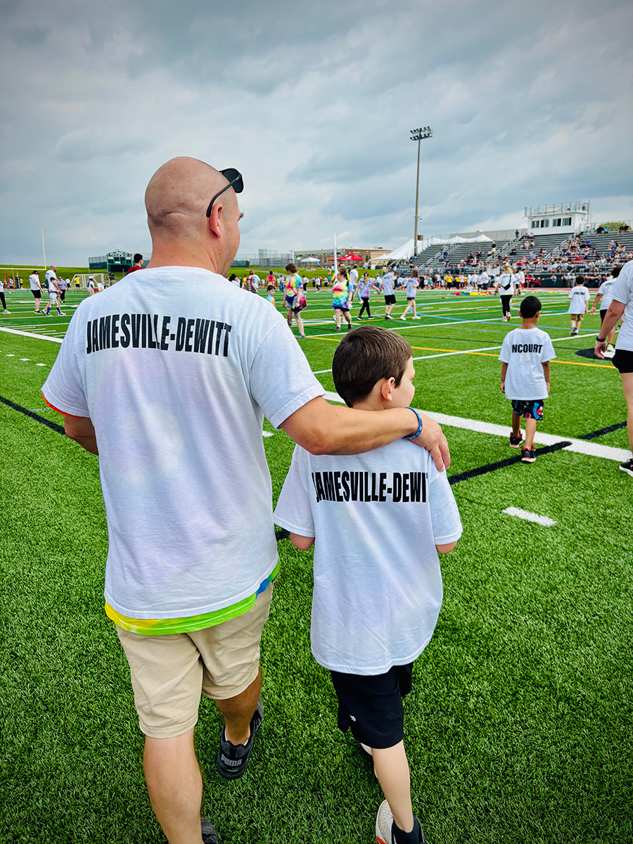 Tecumseh teacher walks with students at special olympics wearing white shirts with Jamesville-DeWitt written on the back.