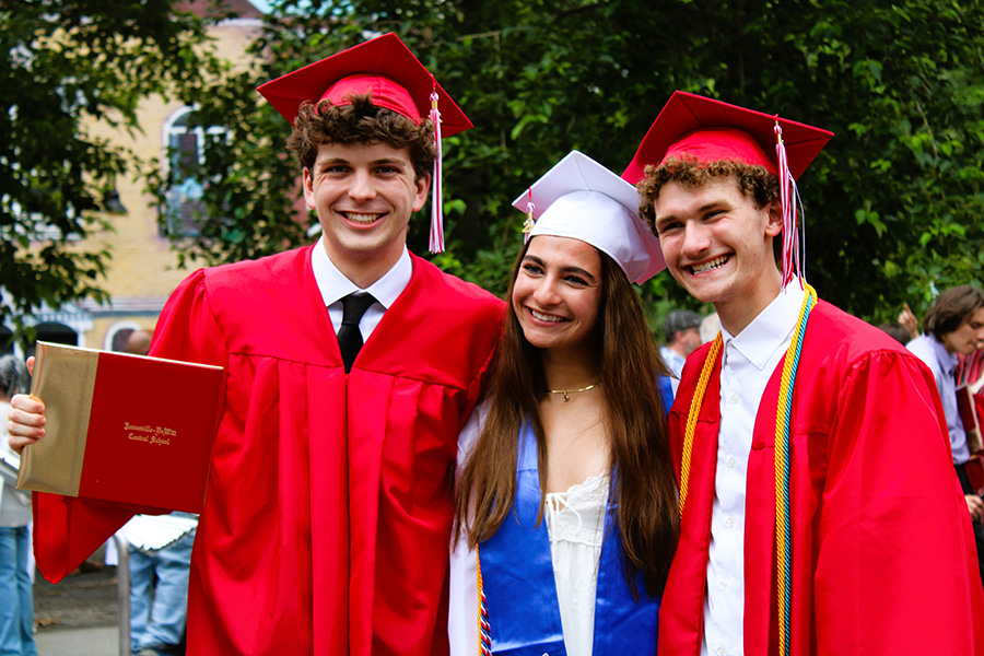 Three graduates pose for photos with diploma wearing caps and gowns.