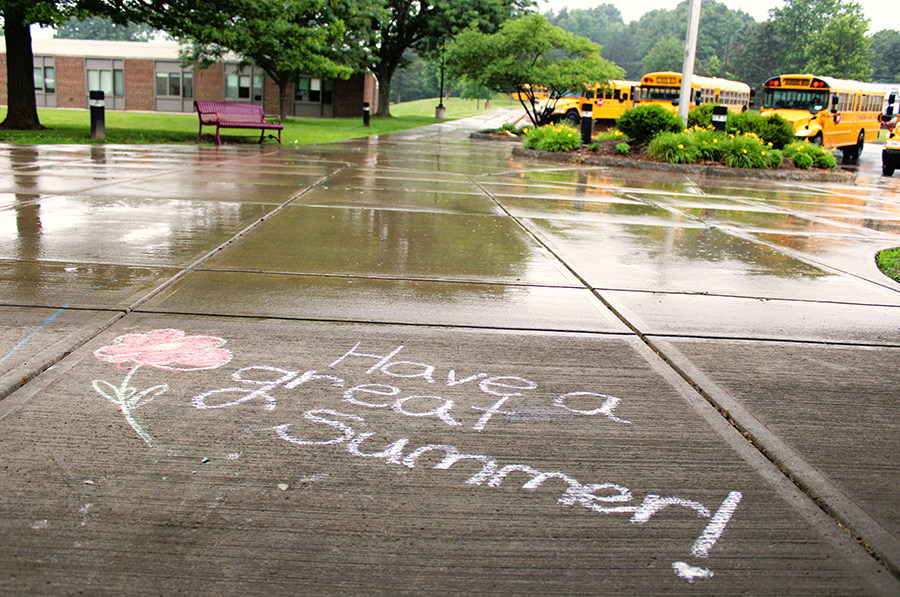 Chalk message on the ground outside the middle school reads, "Have a great summer!" with school buses in the background.