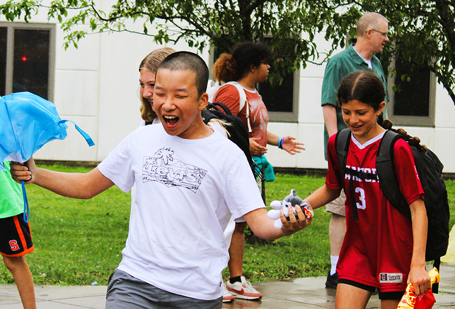 Middle school students smile with excitement while walking to school buses on last day of school in the rain.