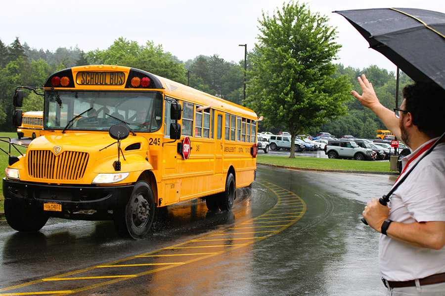 Middle school principal waves to students on buses leaving school grounds.