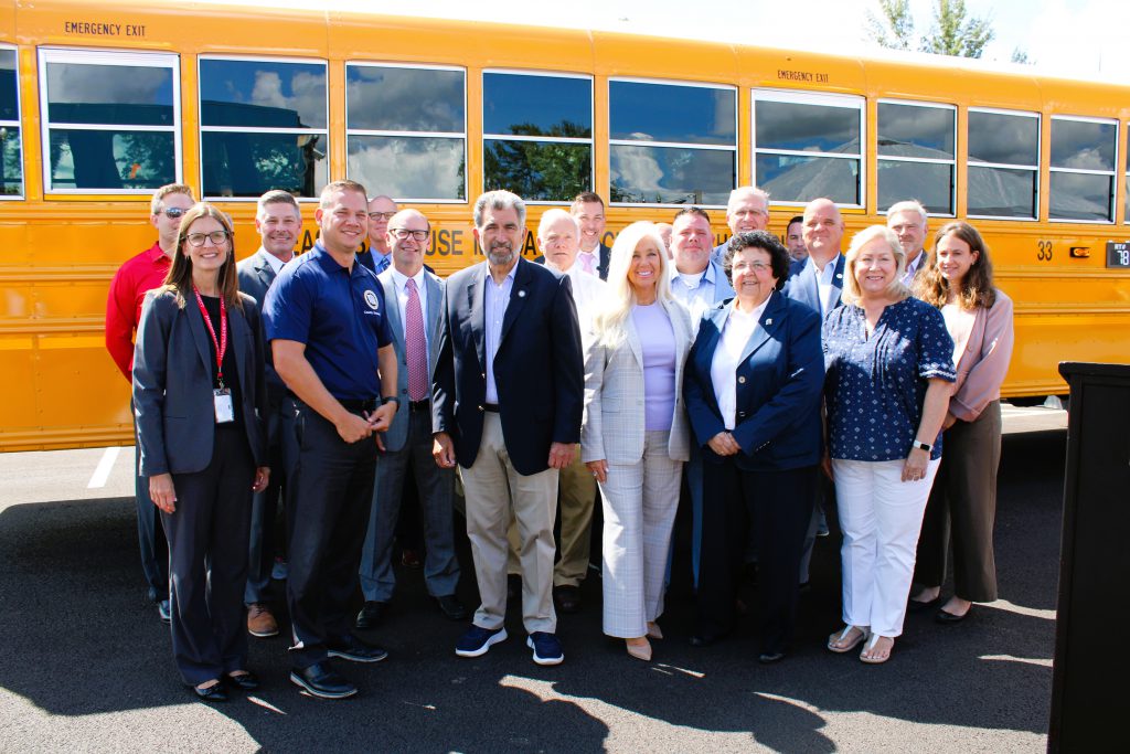 Area Superintendents pose for group photo with county executive in front of school bus.