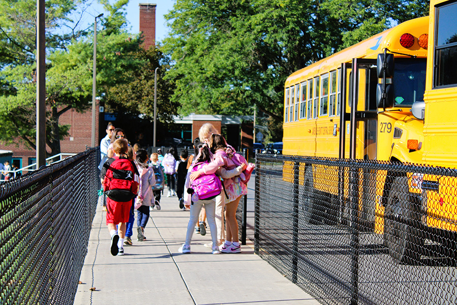 Staff member hugs students as they get off the bus.