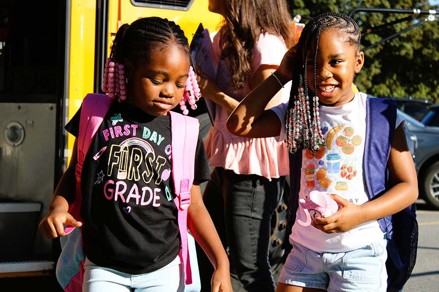 Students smile towards camera while getting off bus.