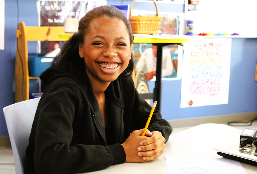 Student smiles while doing assignment at desk.