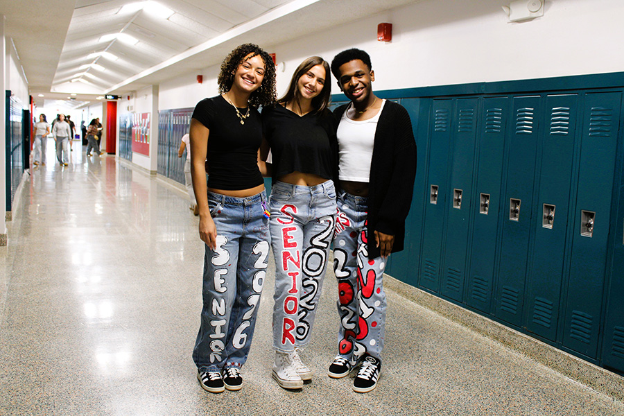 Three seniors pose for photo in hallway of school wearing painted jeans.