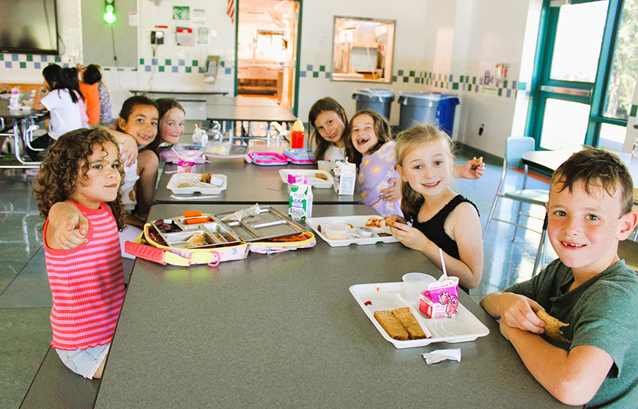 Students sitting around lunch table smile for group photo.