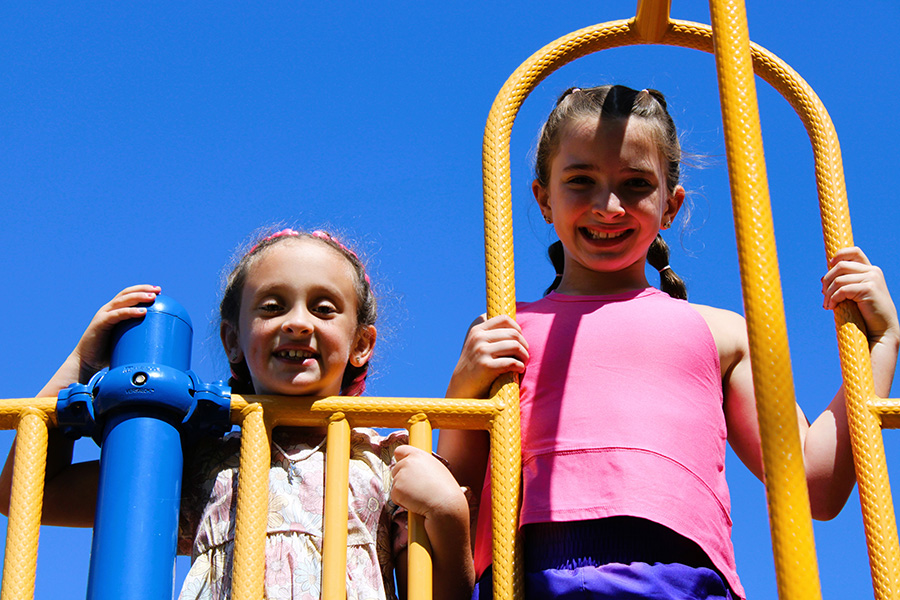 Two students smile for photo on playground equipment.