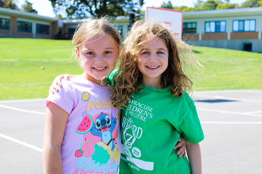 Two students pose smiling outside on basketball court.