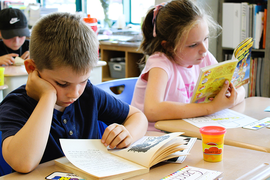 Two students read books at desks. 