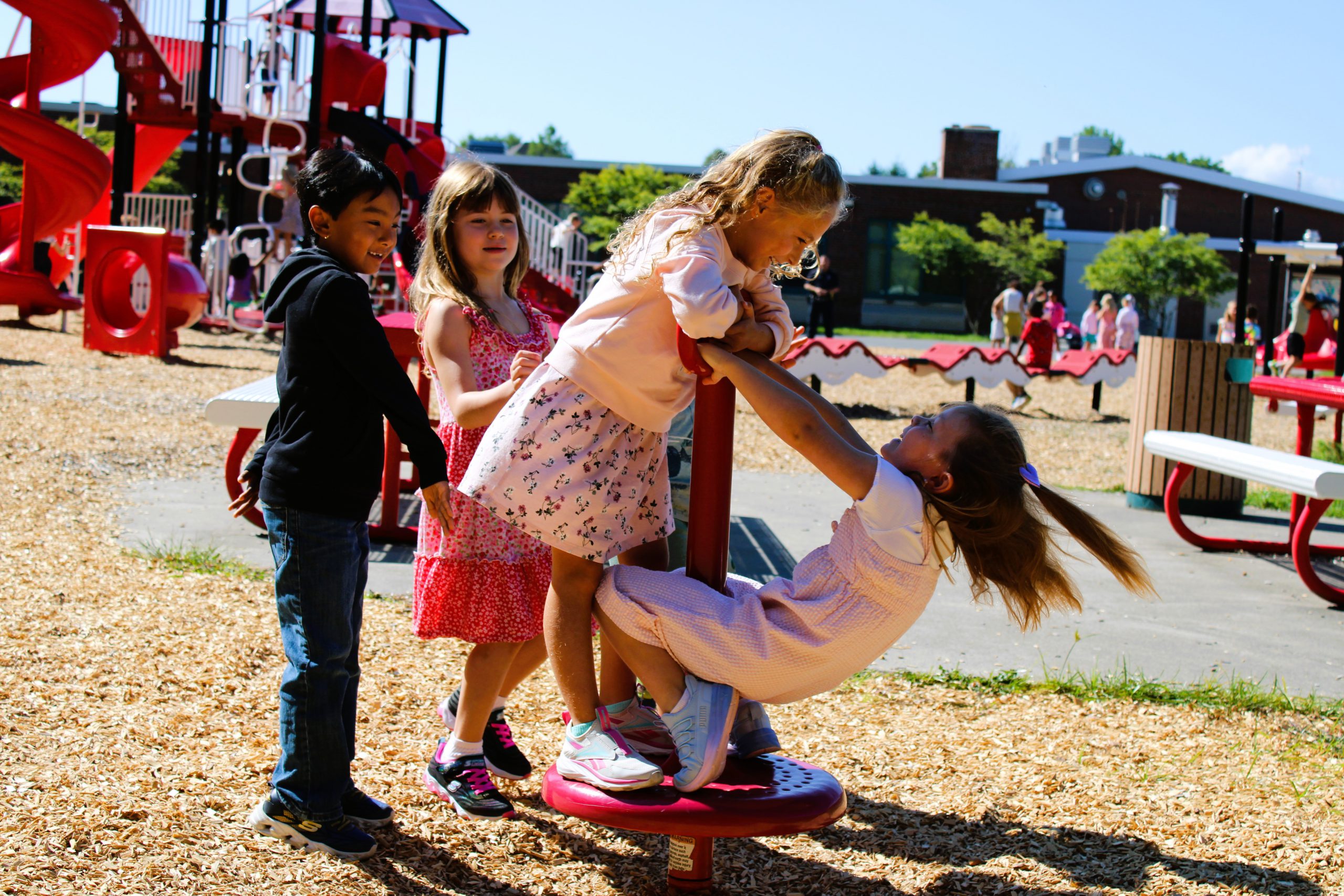 Four students smile while playing on playground equipment.
