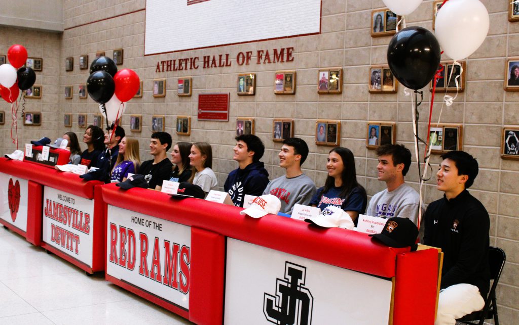 12 student-athletes sit behind table with balloons on National Signing Day.