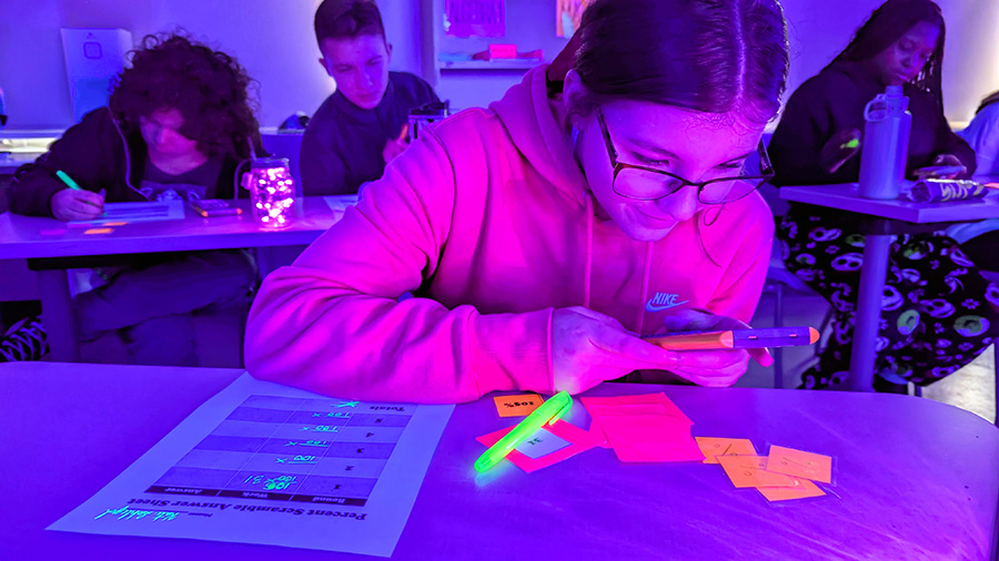 Student does math work at desk with blacklight lighting.