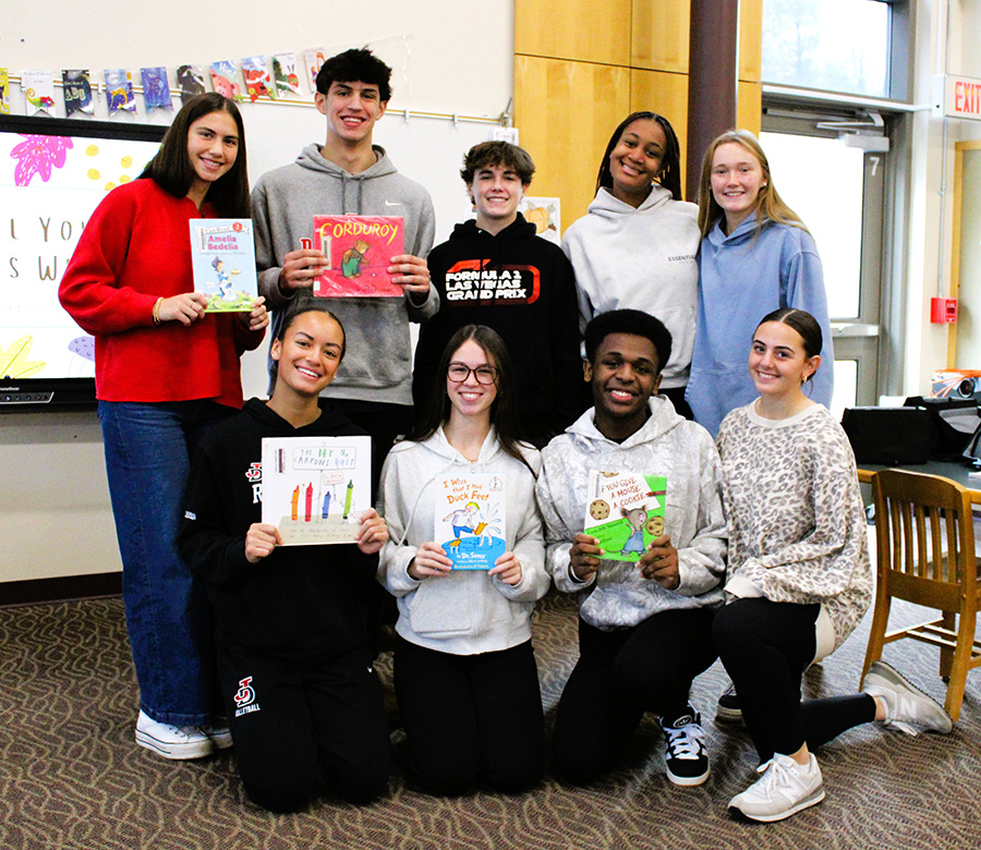 High school students pose for group photo holding children's books.