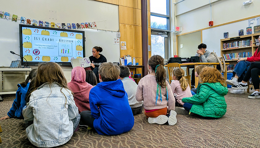 Senior reads to elementary students in library.