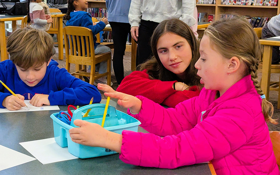 High school student listens to elementary student talking while drawing.
