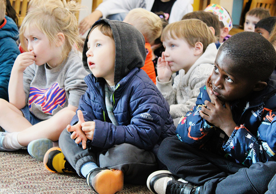 Elementary students sit on the floor listening to story.