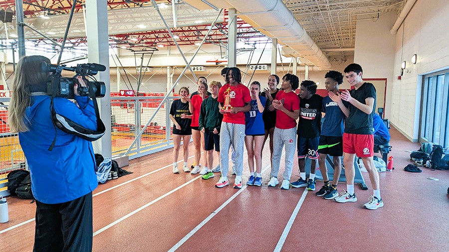 Track and Field team cheer on Amar Lopez as he holds trophy during news filming.