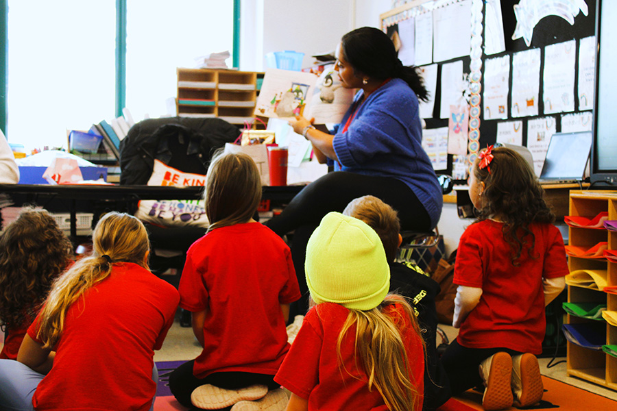 Teacher reads book to students sitting on rug.