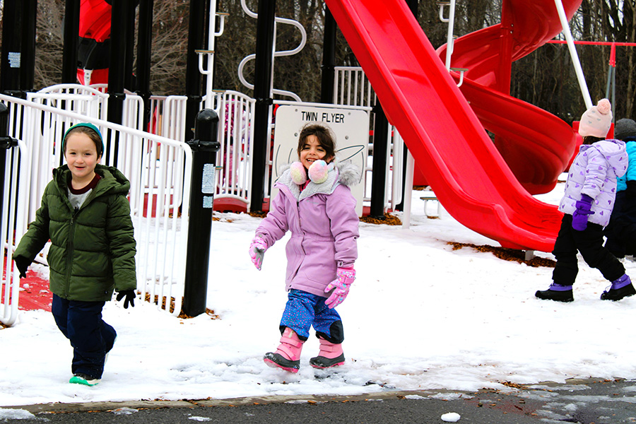 Two students walk on snowy playground smiling towards camera.
