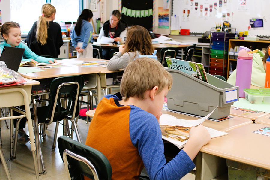 Students read books at desks in classroom.