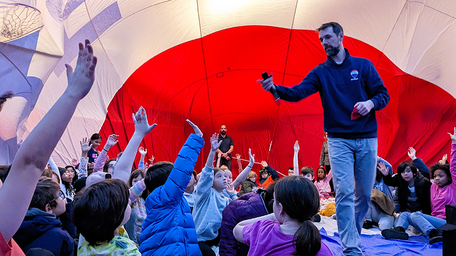 Students raise hands to answer questions while sitting inside hot air balloon.
