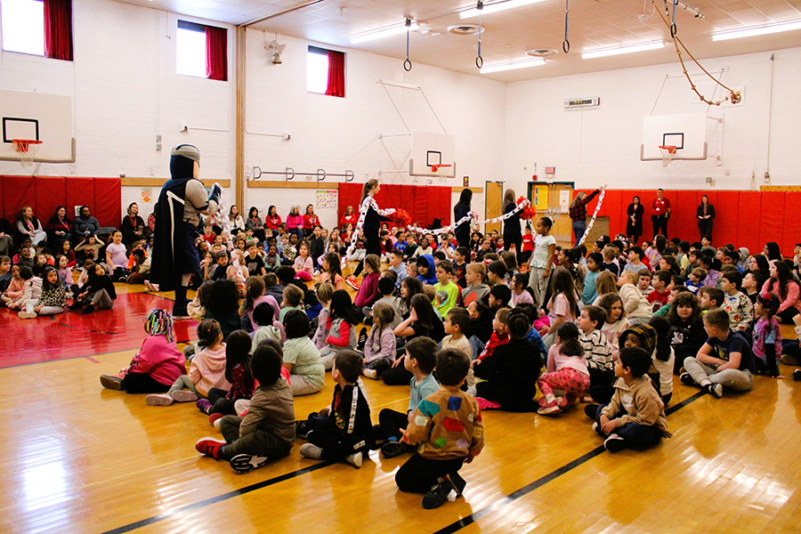 Students sit on floor during assembly and watch a paper kindness chain walked by.