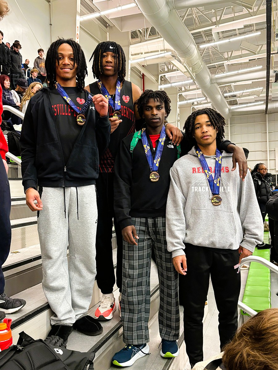 Four students stand in bleachers with medals.