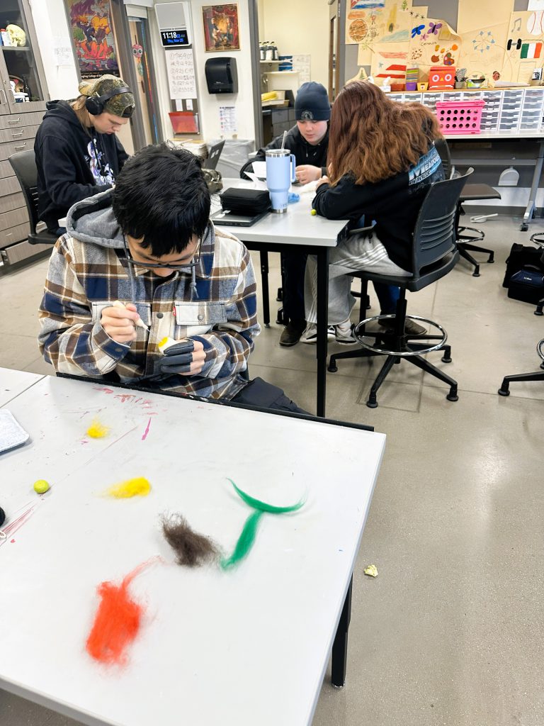 Students work on needle felting project at desks.