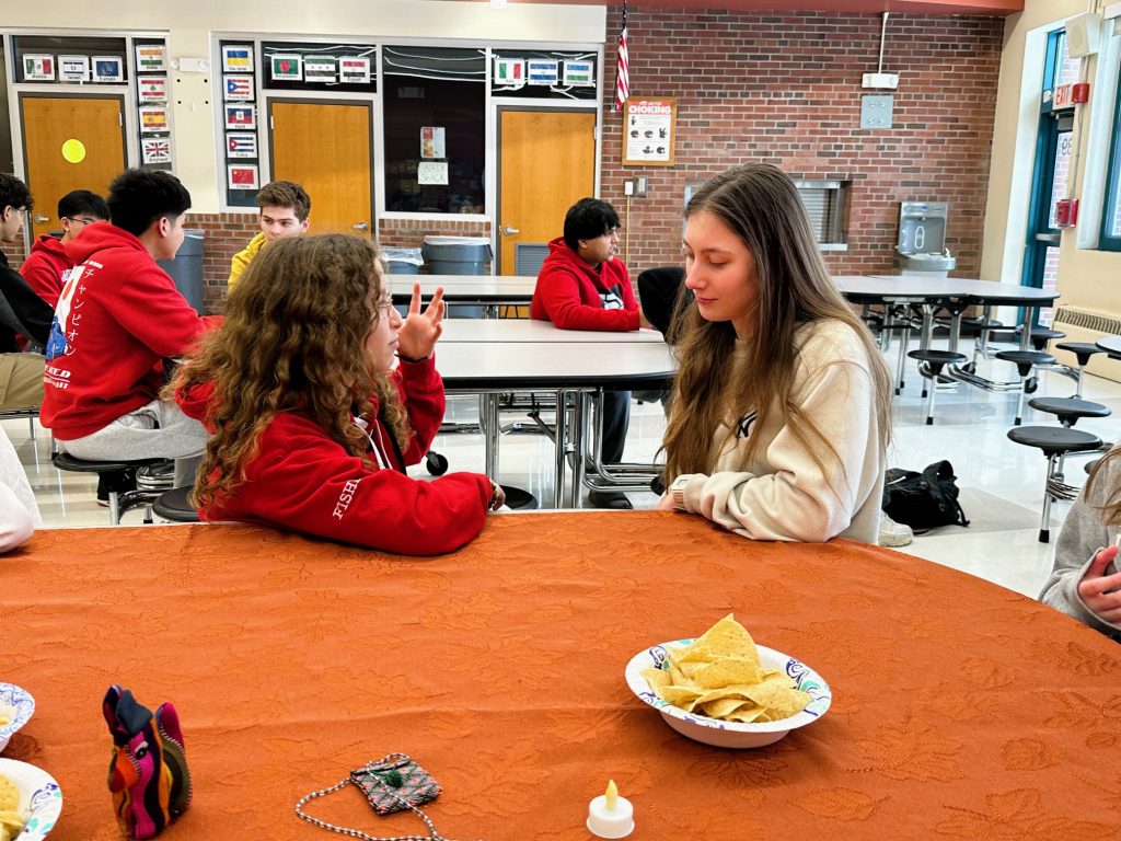 Students sit at cafeteria tables and have a conversation.