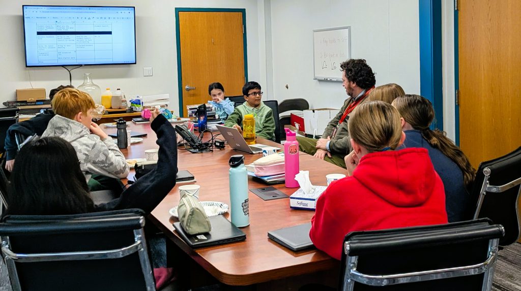 Middle school students sit around conference table with principal.