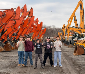 Five students stand in front of heavy equipment with thumbs up.